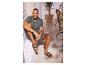 Homme en chemise verte et short, assis dehors en sandales.