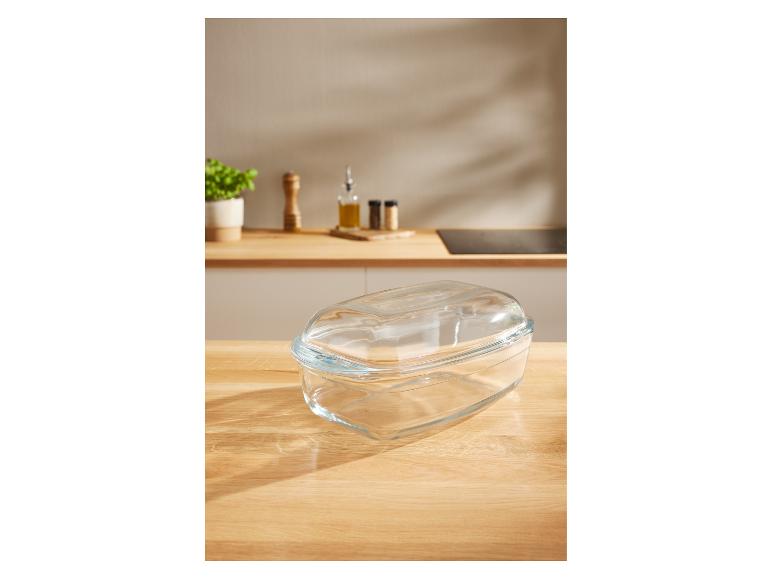 Plat de cuisson en verre avec couvercle sur un comptoir de cuisine avec des épices et une plante.