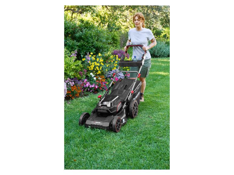 Femme tondant la pelouse avec une tondeuse Parkside dans un jardin fleuri.