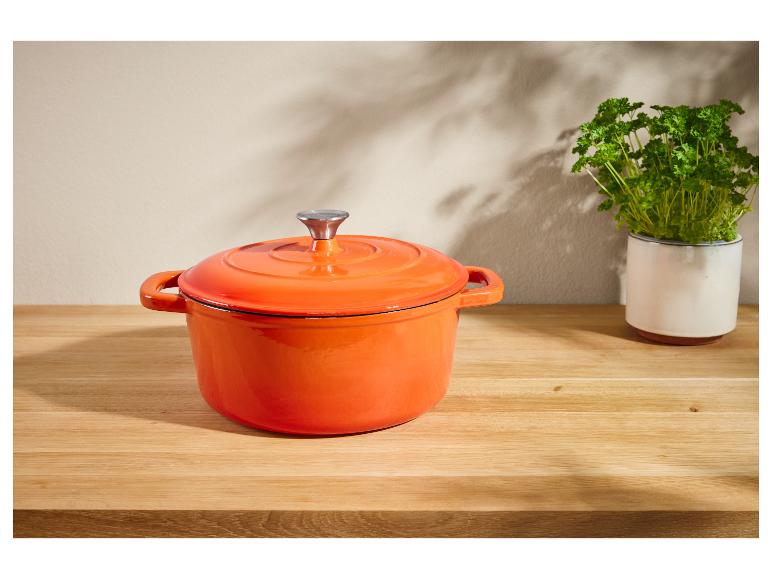 Cocotte orange en fonte sur une table en bois.