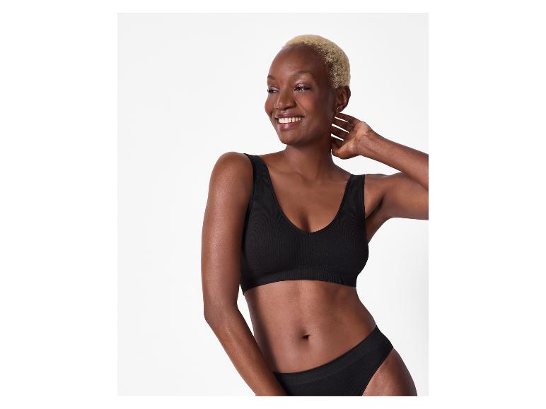 Femme souriante aux cheveux blonds courts portant un soutien-gorge et une culotte côtelés noirs sans couture.