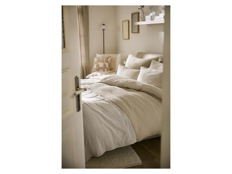 Chambre à coucher lumineuse avec un lit fait de draps et d'oreillers beiges et blancs.