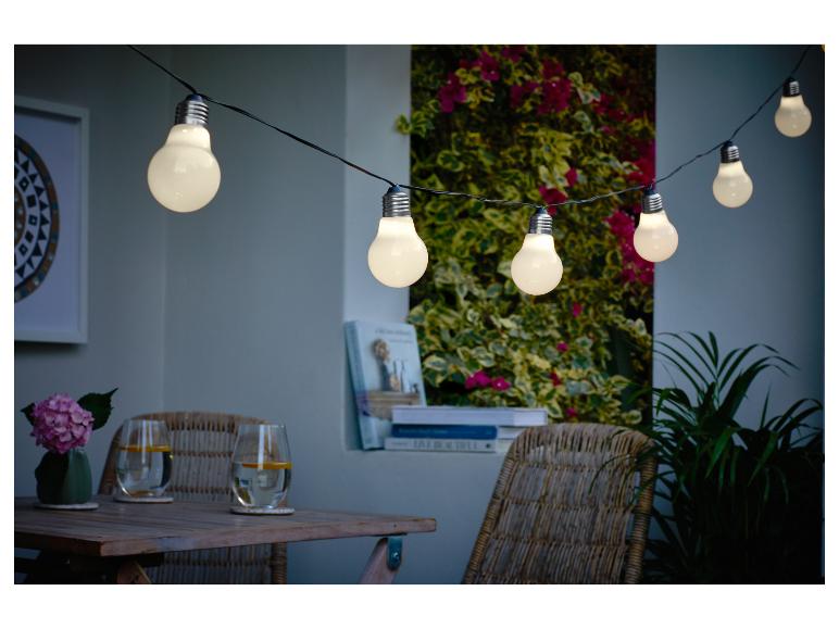 Guirlande lumineuse extérieure éclairant un patio confortable avec table en bois et chaises en osier.