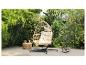 Chaise suspendue en rotin avec coussins crème sur une terrasse entourée de verdure.