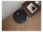 Aspirateur robot noir sur parquet en bois à côté d'une table de chevet avec un livre et des vases.