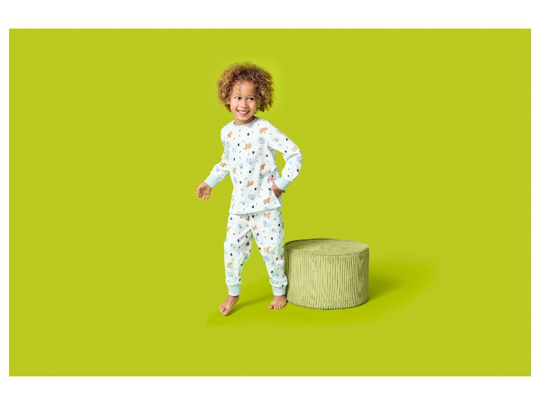 Enfant heureux en pyjama blanc à motifs d'ours et de nuages, à côté d'un pouf vert.