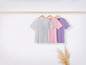 Trois t-shirts en gris, rose et violet sont suspendus à un cintre en bois.