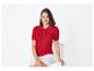 Femme en polo côtelé rouge et short blanc, assise sur une chaise blanche.