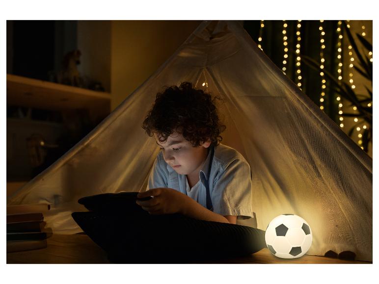 Un garçon lit un livre dans une tente avec un ballon de football lumineux.