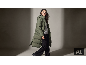 Femme en long manteau matelassé vert, pull gris et pantalon noir