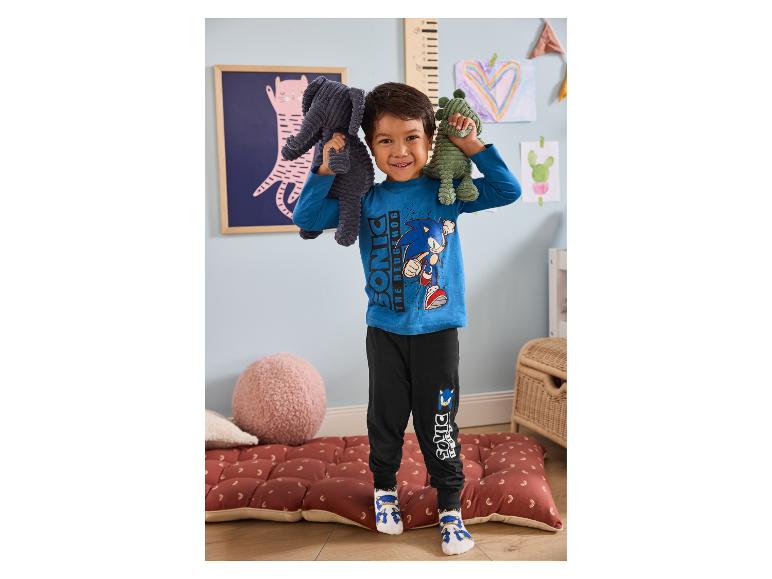 Garçon souriant en pyjama Sonic the Hedgehog tenant deux peluches dans une chambre ludique.