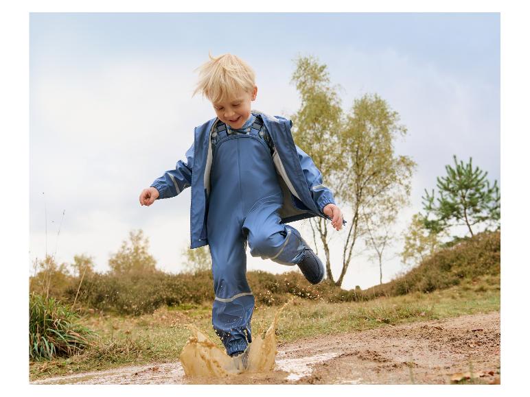 Enfant heureux en tenue imperméable bleue sautant dans une flaque de boue en extérieur.