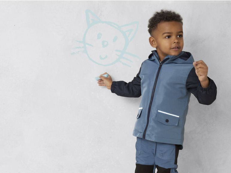 Un garçon portant une veste bleue dessine un chat sur un mur blanc.