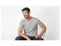 Homme en t-shirt gris et jean foncé, assis sur une chaise, souriant.