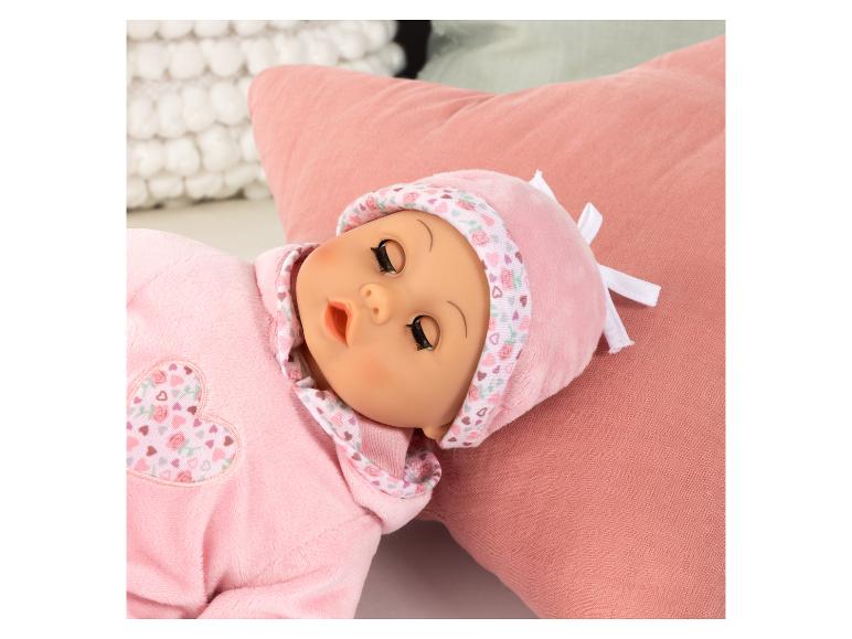Une poupée en pyjama et bonnet roses avec des cœurs et des roses, allongée sur un coussin rose.