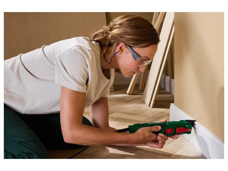 Une femme utilise un outil multifonction vert et rouge pour couper une plinthe blanche.