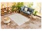 Tapis beige à motifs, canapé et pouf en rotin pour une terrasse extérieure.