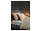 Coin chambre avec un lit en tissu gris, deux oreillers couleur pêche et une lampe de chevet.