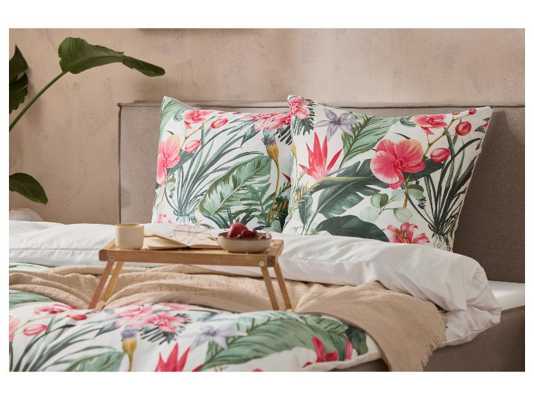 Lit avec housse de couette et oreillers à motifs floraux tropicaux, plateau de petit-déjeuner avec café et fruits.