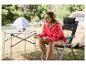 Femme assise sur une chaise de camping pliable, lisant une carte près d'une table de camping.