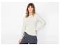 Femme en blouse claire à manches longues et jean foncé, posant sur fond blanc.