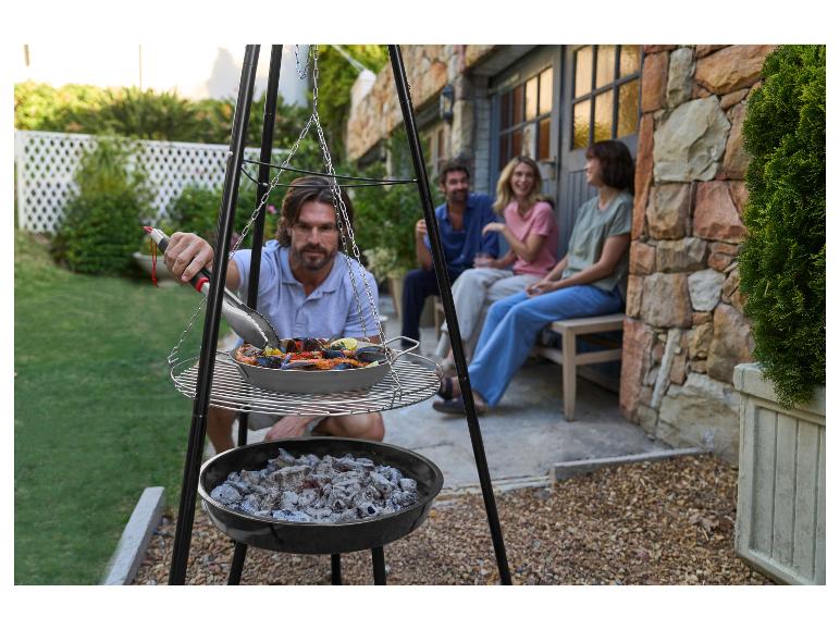 Homme faisant griller des fruits de mer sur un barbecue trépied avec des amis en arrière-plan.
