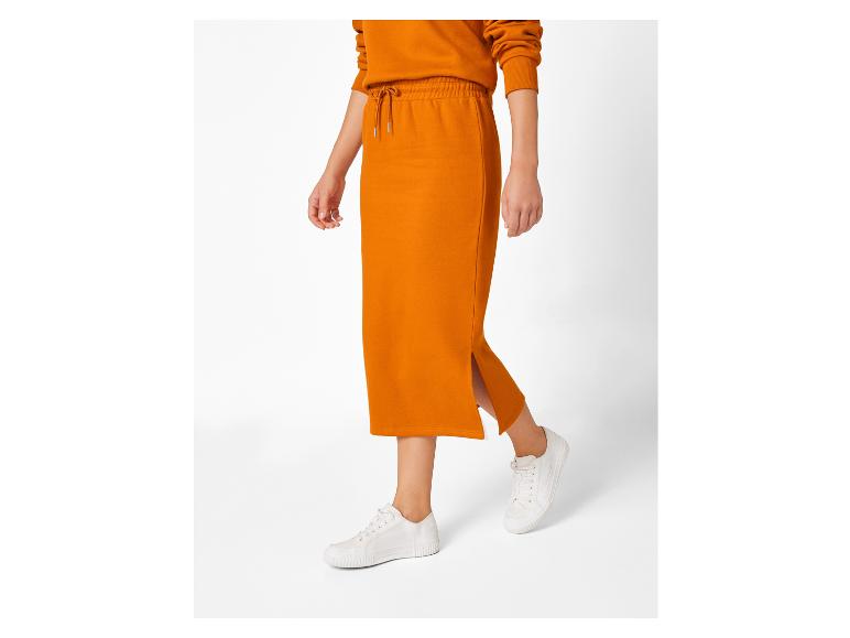 Une femme portant une jupe orange et des baskets blanches.