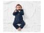 Un bébé souriant allongé sur une couverture blanche dans une combinaison bleu marine.