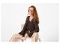 Femme en cardigan tricoté marron et pantalon beige, assise sur une chaise.