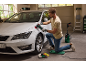 Un homme polit une voiture blanche avec une polisseuse rotative dans un garage.