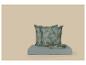 Coussins verts et draps pliés à motif de feuilles sur une plateforme bleu clair.