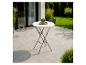 Table de bistrot blanche avec plante sur une terrasse donnant sur un jardin.