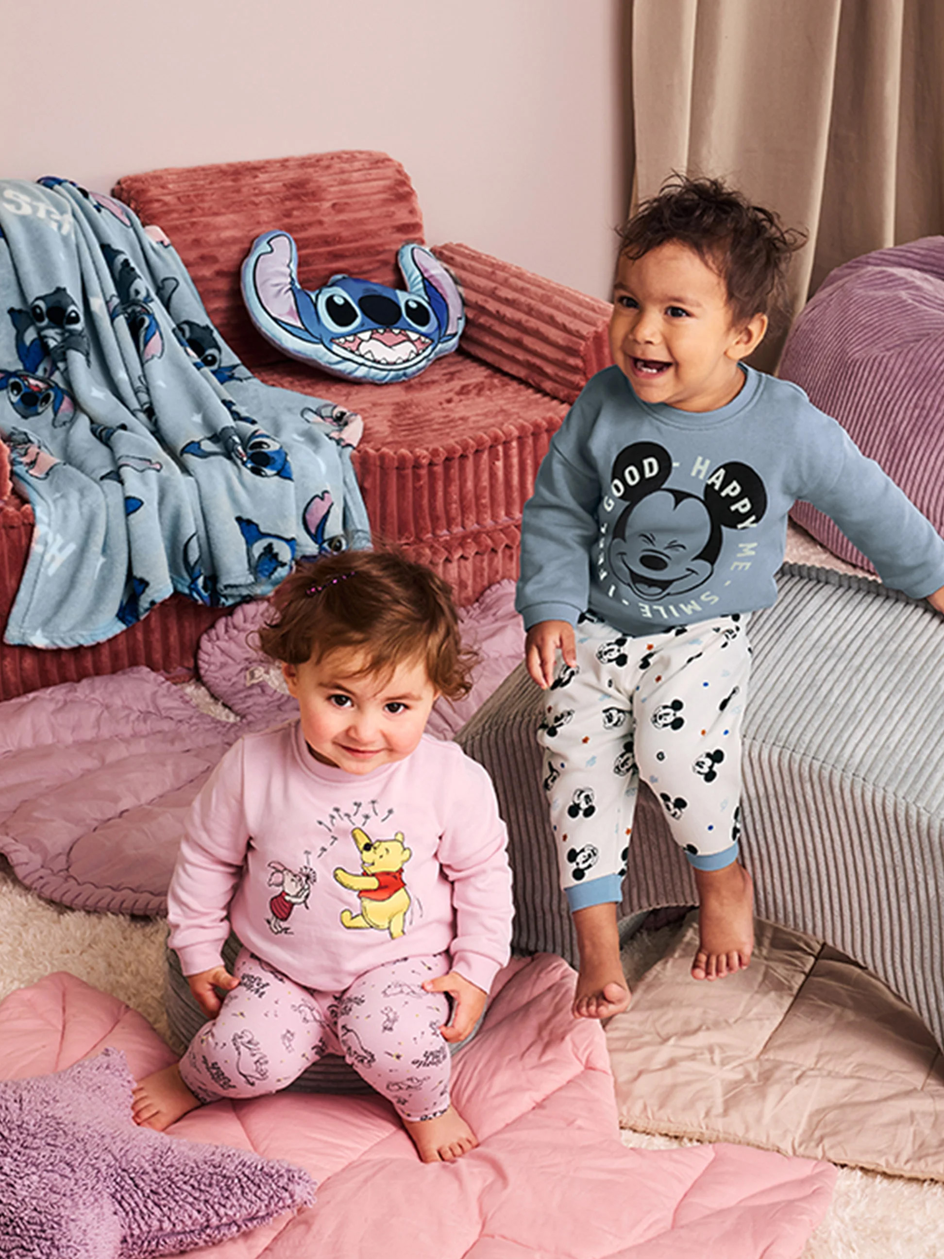 Deux bébés en pyjama Disney, entourés de couvertures et oreillers Stitch.