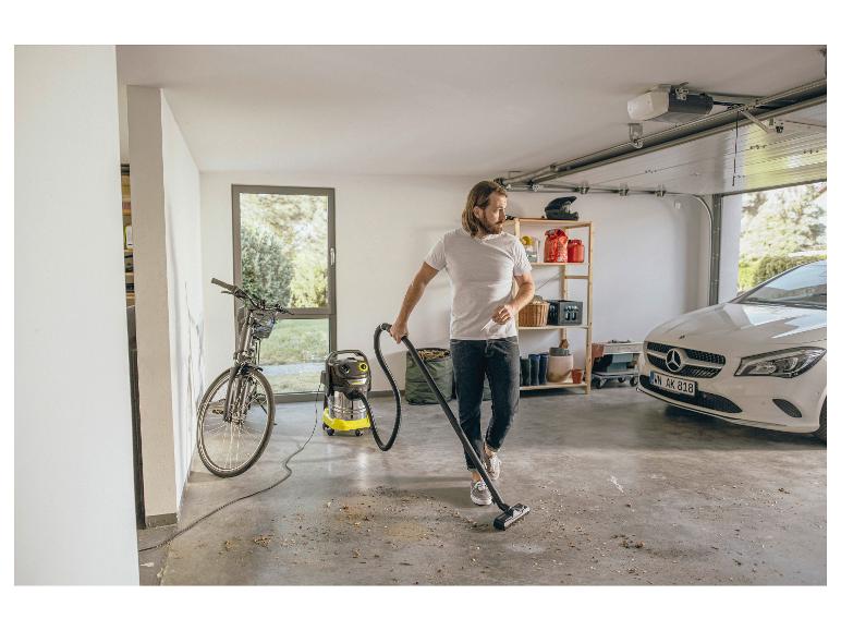 Homme aspirant le garage avec un aspirateur eau et poussière, avec un vélo et une voiture en arrière-plan.