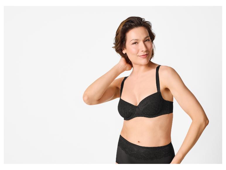 Femme en soutien-gorge et culotte noirs en dentelle, souriant à la caméra.