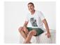 Homme en t-shirt blanc imprimé palmiers et short vert assis sur un pouf.