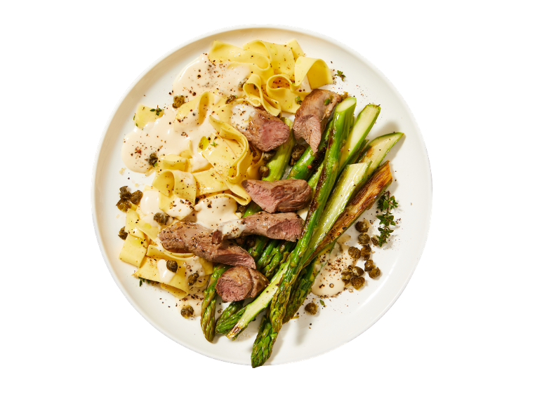 Pappardelle avec sauce crémeuse, bœuf, asperges et câpres sur une assiette blanche.