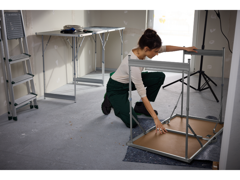 Une femme assemble une table pliante dans une pièce en construction.