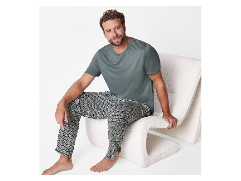 Un homme assis sur un fauteuil moelleux, vêtu d'un t-shirt vert foncé et d'un pantalon à motifs.