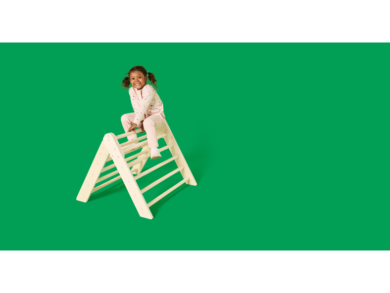 Enfant joyeux en pyjama assis sur un triangle d'escalade en bois.