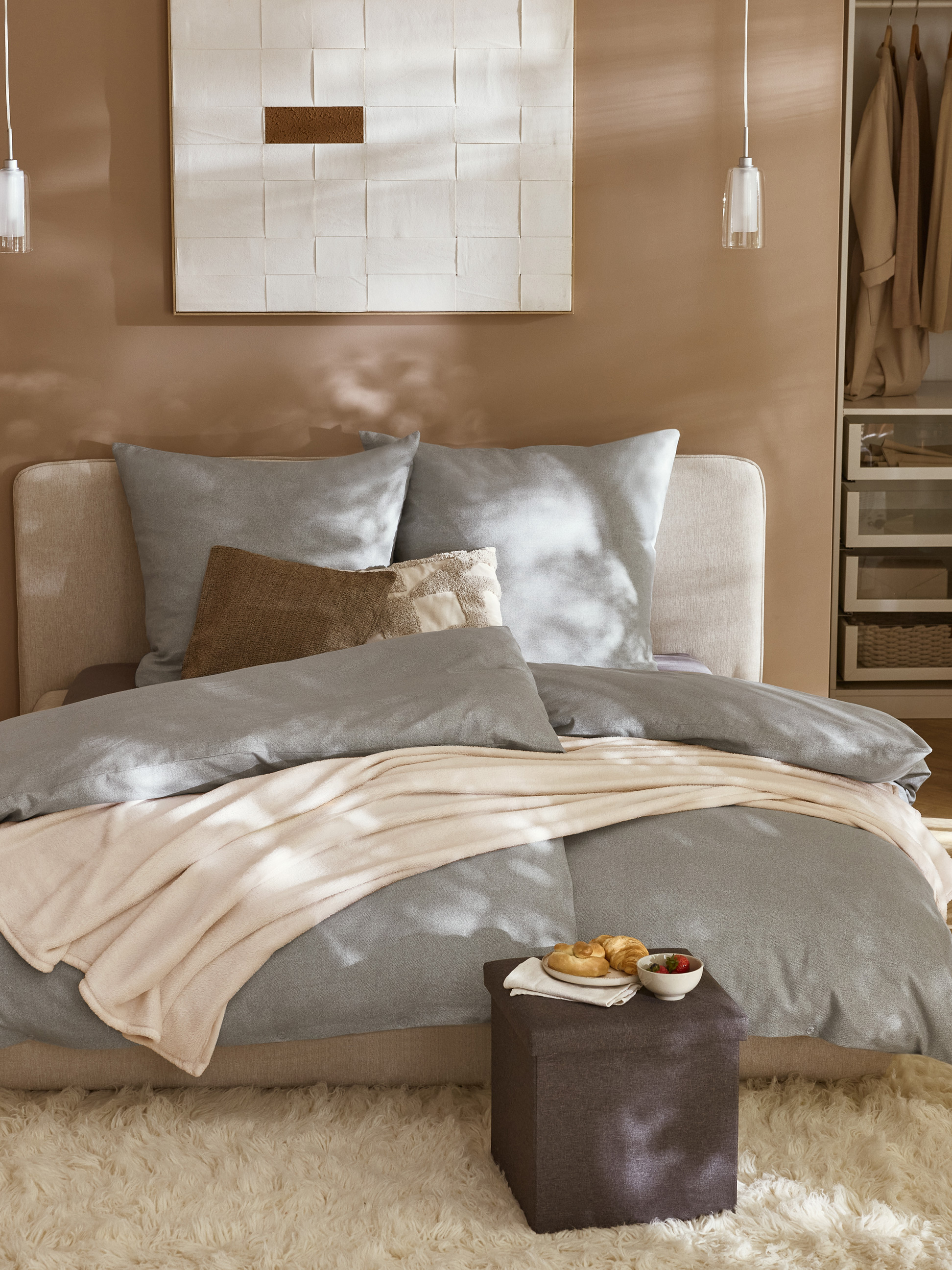 Chambre à coucher confortable avec lit gris, plaid beige et pouf marron avec petit-déjeuner.