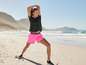 Une femme en short rose et un t-shirt noir fait du yoga sur la plage.