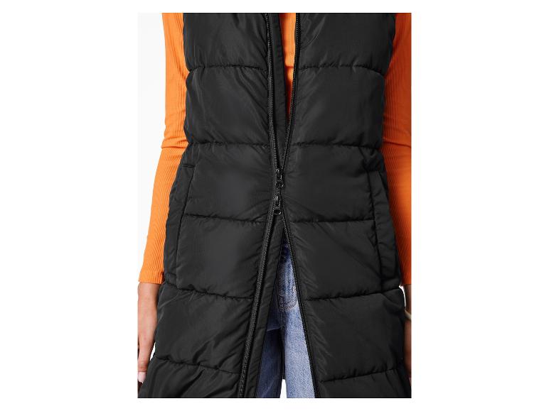 Long gilet matelassé noir avec une chemise orange à manches longues et un jean.