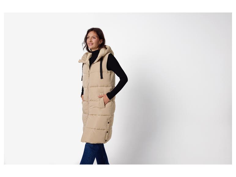 Femme en longue doudoune sans manches beige à capuche, pull noir et jean foncé