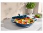 Cocotte bleue avec couvercle remplie de légumes coupés, à côté d'un plant de basilic.
