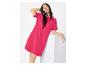 Femme en robe t-shirt fuchsia, appuyée sur un bloc blanc.
