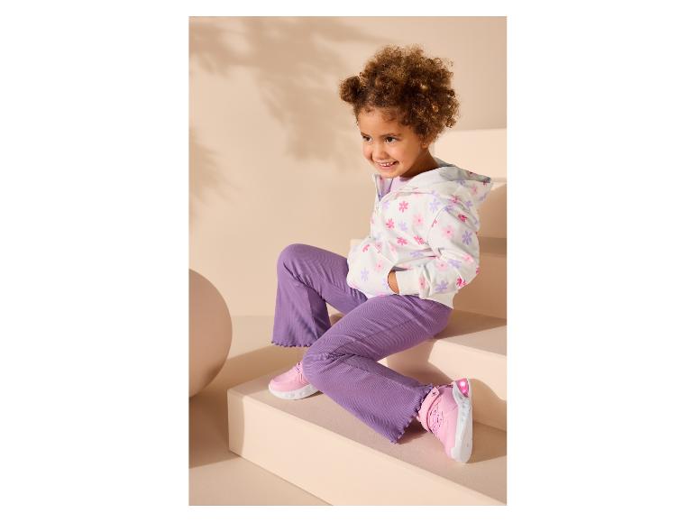 Fille en sweat à capuche blanc fleuri et pantalon violet, assise sur des marches