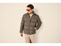 Homme en doudoune gris foncé, pull beige clair et pantalon beige clair.