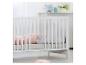 Lit bébé blanc avec literie rose et oreillers en peluche dans une chambre lumineuse.