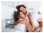 Un couple s'embrassant dans un lit avec des draps blancs, avec le logo Häussling.